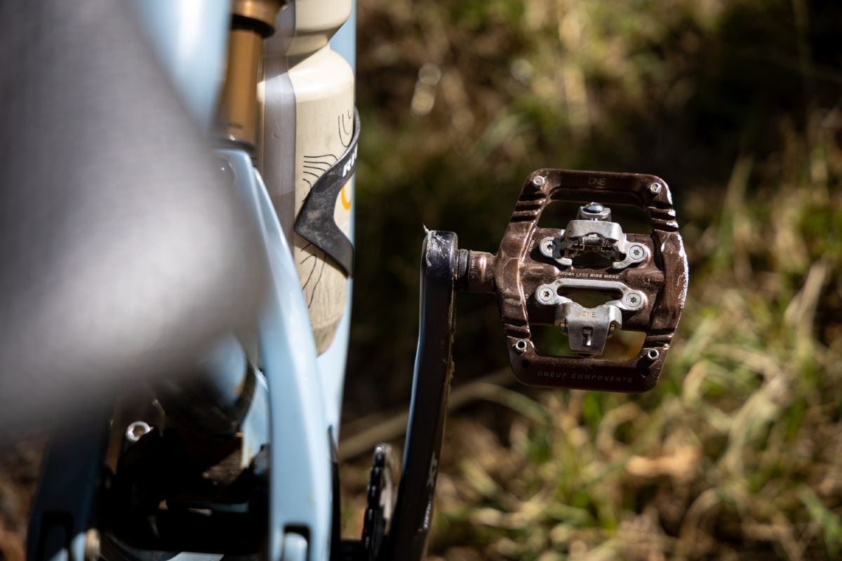 OneUp Components CLIP pedal mounted to a bike with text work less ride more visible