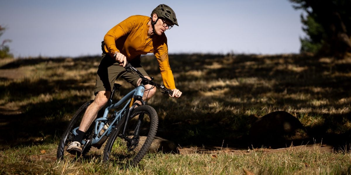a mountain bike rider taking a sharp turn amidst grass, rocks and trees